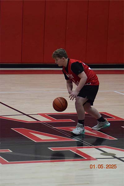 young boy in red dribbling up the court