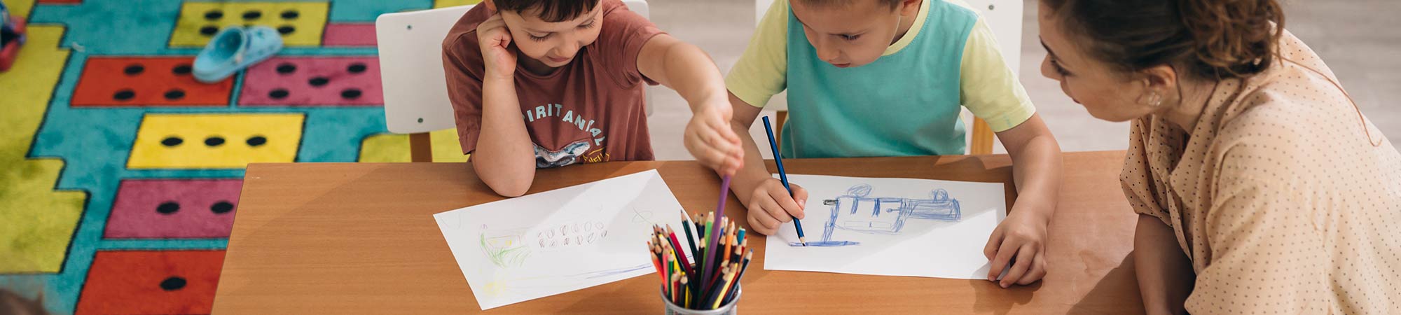 Two students drawing with a teacher at a table