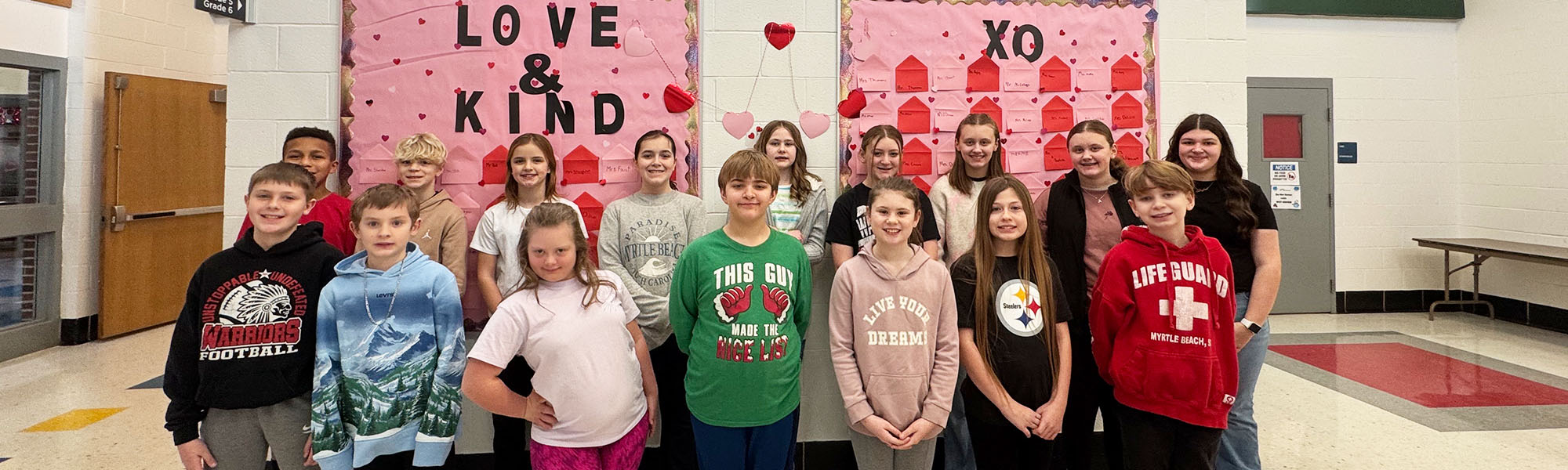 Group of happy elementary students in front of a Love & Kind bulletin board