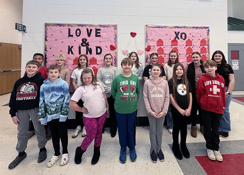 Group of happy elementary students in front of a Love & Kind bulletin board