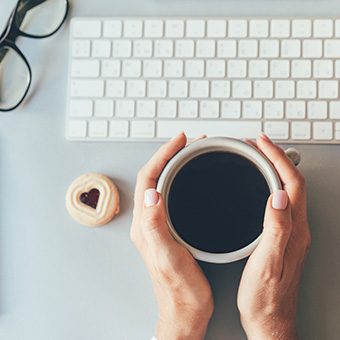 Teacher holding a cup of coffee next to keyboard and heart-shaped cookie