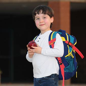 Kindergarten student holding an apple and wearing a backpack
