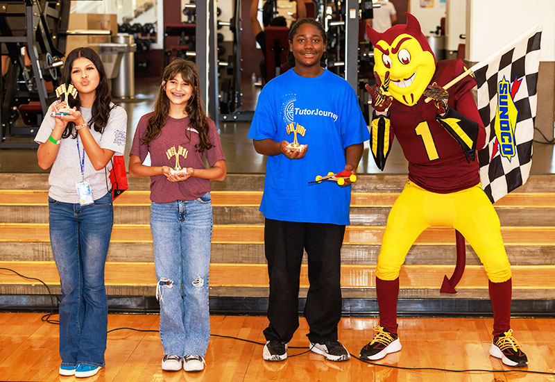 Three happy students holding awards next to school mascot