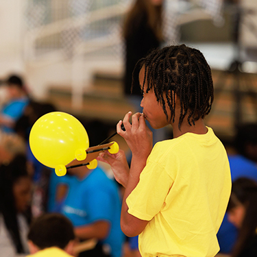 Student in yellow blowing up a balloon for a project