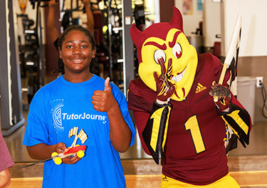 Student smiling next to mascot and giving a thumbs up