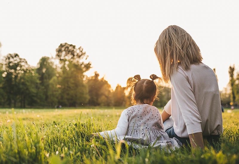 Mother with child sitting in a grassy area in the sun