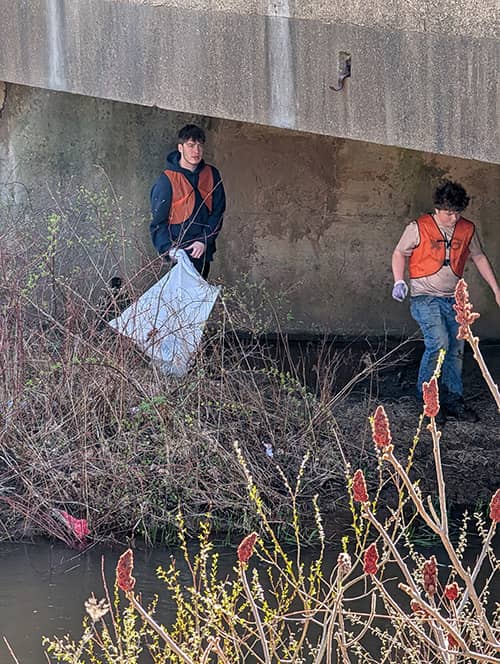 Students cleaning trash under an embankment area