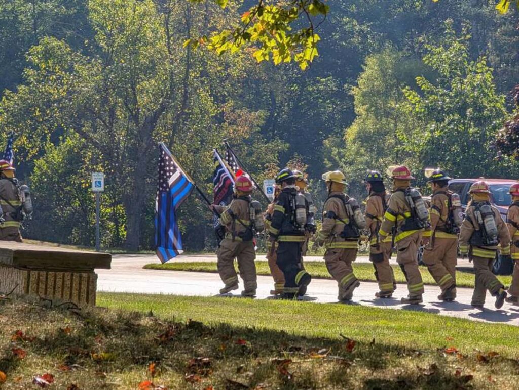 Homeland security students dressed in gear and proudly holding up USA flags while walking down a road