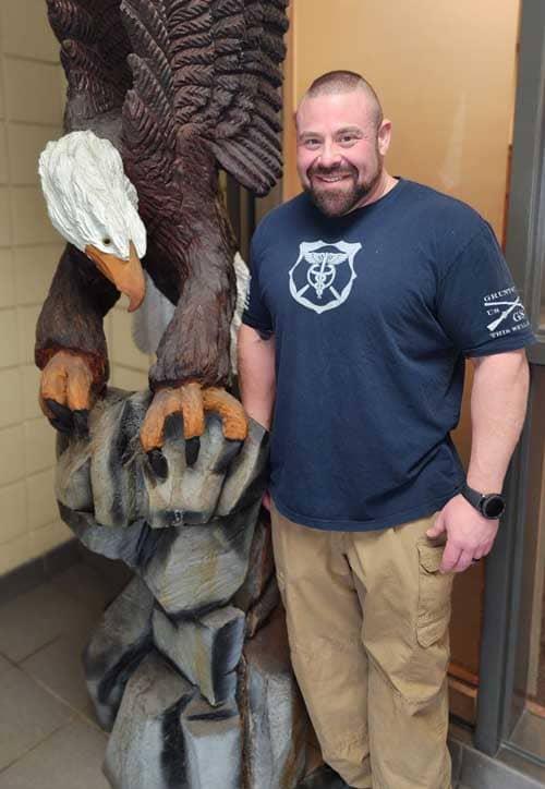 Christopher Schwab standing next to a carved eagle