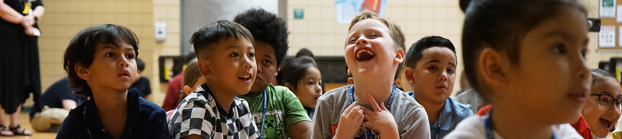 Happy elementary students sitting on the gym floor enjoying a presentation