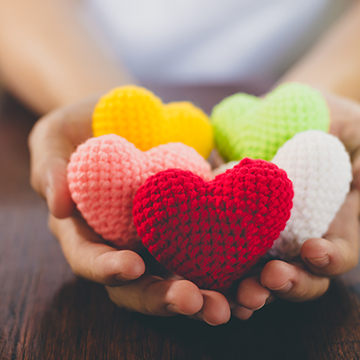 Hands holding colorful, knitted hearts