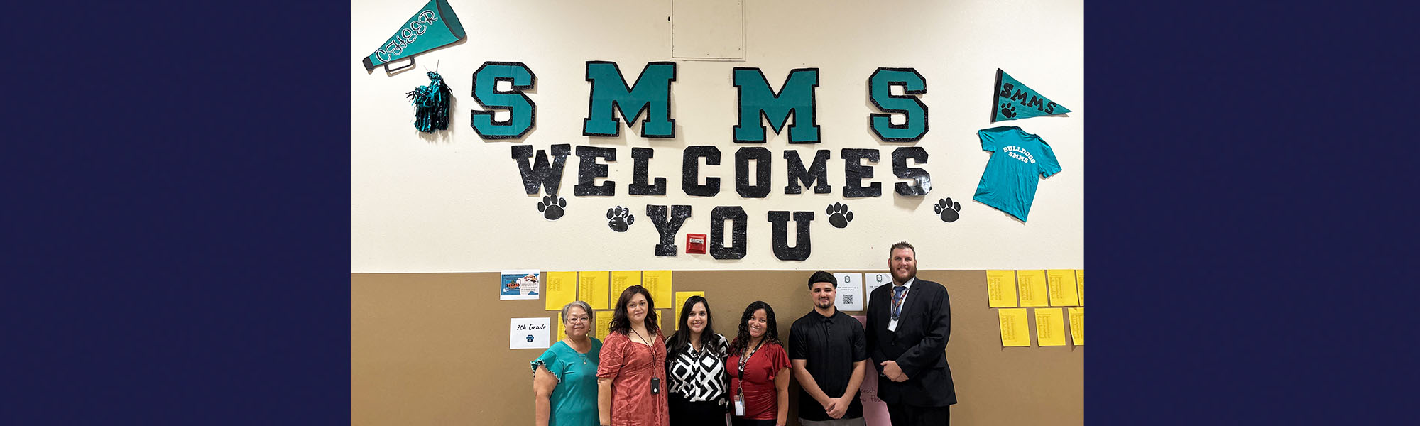 Group of happy school staff members under SMMS Welcomes You banner