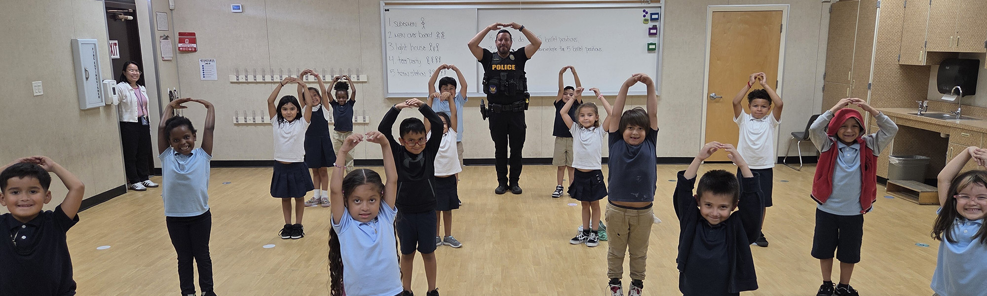 Sunrise Ms. Chaparro's dance class: a policeman and children with their hands raised over their heads in an arc