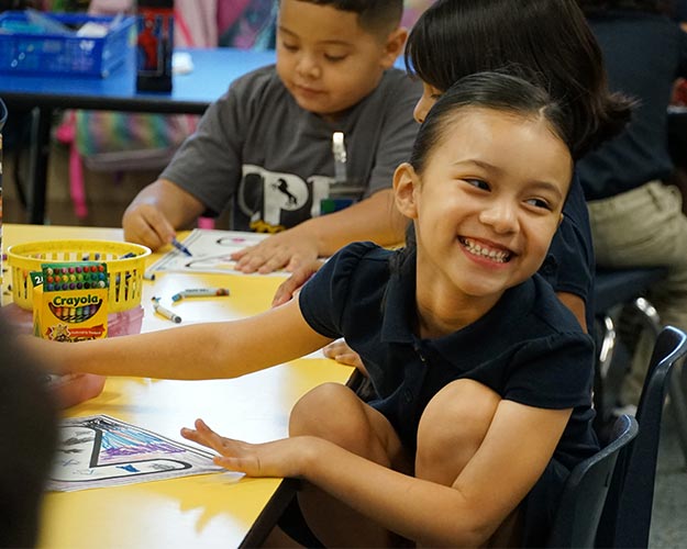 Student smiling at a table and coloring with crayons
