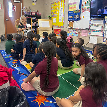 Students sitting down on a rug and listening to the teacher
