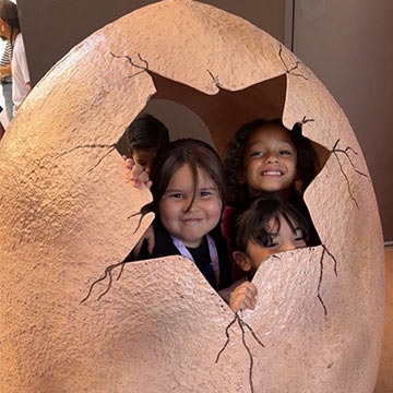 Students peeking out of a giant dinosaur egg