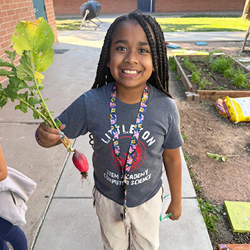 sidebar_AboutUs_110518 Happy female student holding up a radish from the school garden