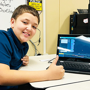 Student looking up from his desk to smile for the camera