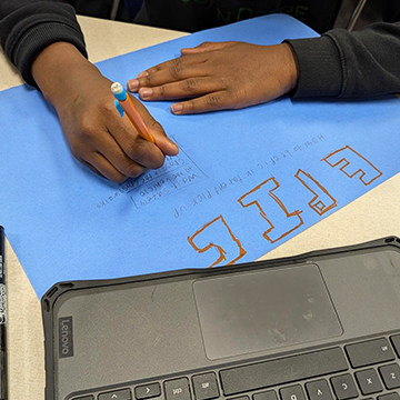 sidebar_AboutUs_110518 Student writing from desk in classroom