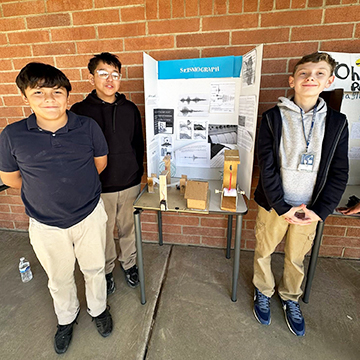 Three middle school boys standing around their project