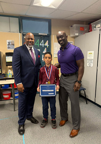 Student holding AASA State Assessment certificate while standing between the superintendent and Littleton STEM principal