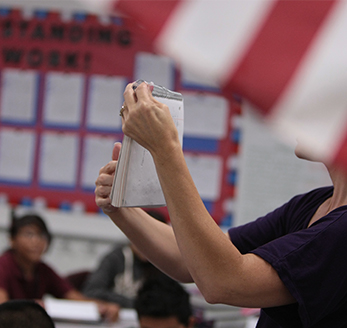sidebar_voterregistration Teacher holds up a book in front of the class