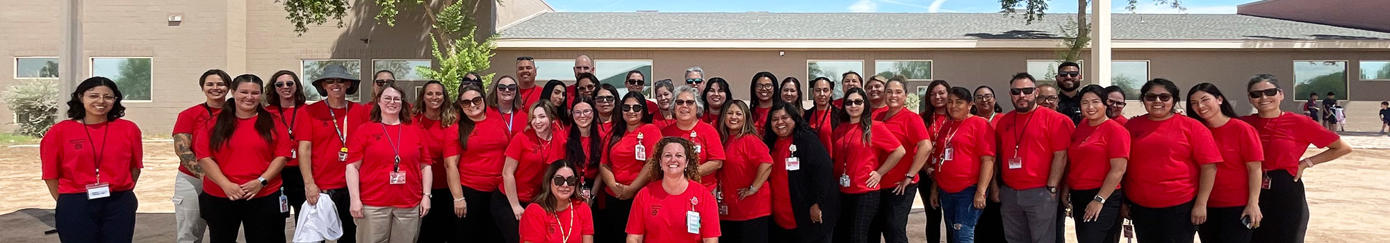 Happy staff members wearing red t-shirts posing for a group photo in front of the school building