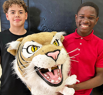 Two students smiling and holding school mascot costume