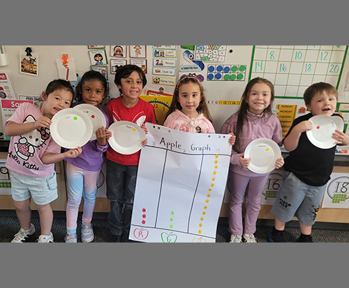 Group of happy Kindergarten students posing for a picture with their apple taste test and graphing projects