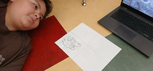 Student looking at his drawing next to a laptop