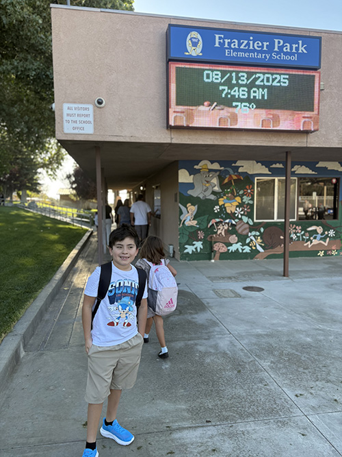Happy school boy smiling in front of Frazier Park school sign