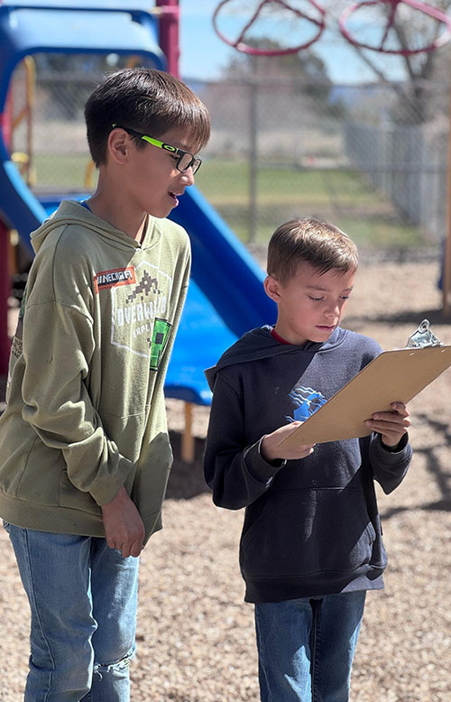 Two students working on a project outside and holding a clipboard