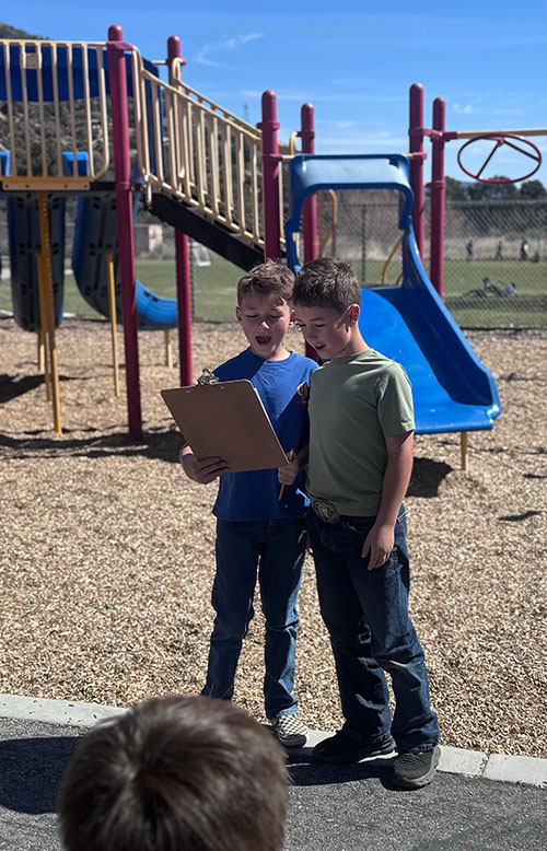Two third grade boys reading from a clipboard