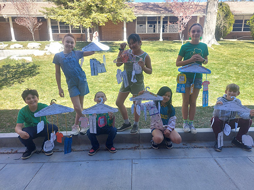 Students holding their final work in a unique and eye-catching display using clothing and coat hangers