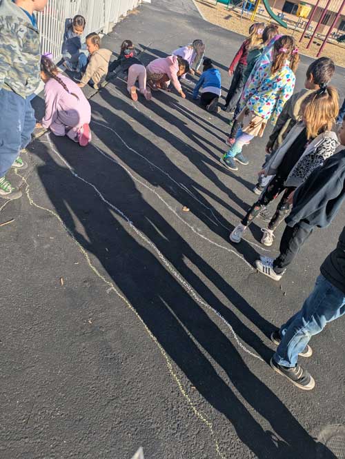 Students watching other students outline their shadow with chalk