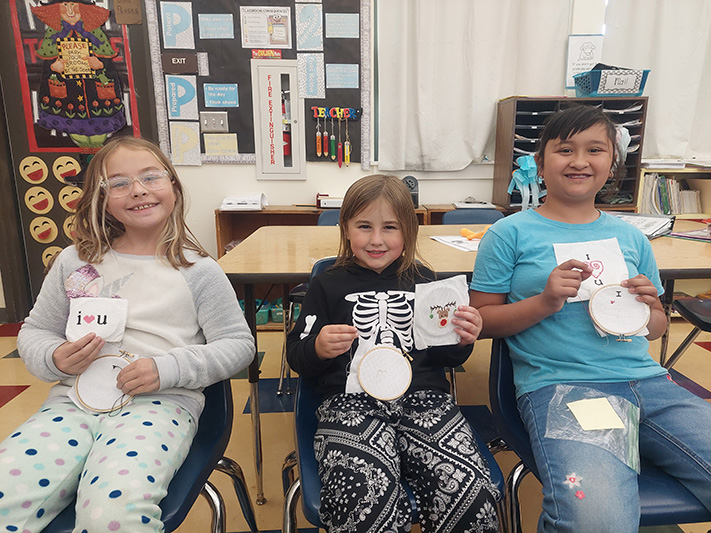 Three girls holding cross stitch projects