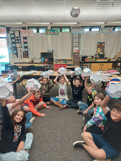 Students sitting on the floor holding up their paper bloom projects