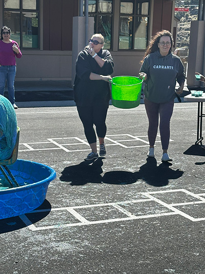 Two staff members carrying a bucket of slime sneaking up behind Principal McNelis
