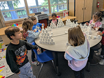 Kindergarten students sitting at a table stacking plastic cups