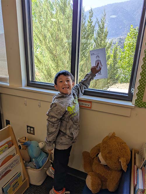student pointing at his drawing in the window