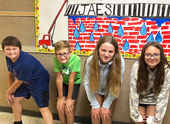 Four spirited students posing for a picture under a school poster