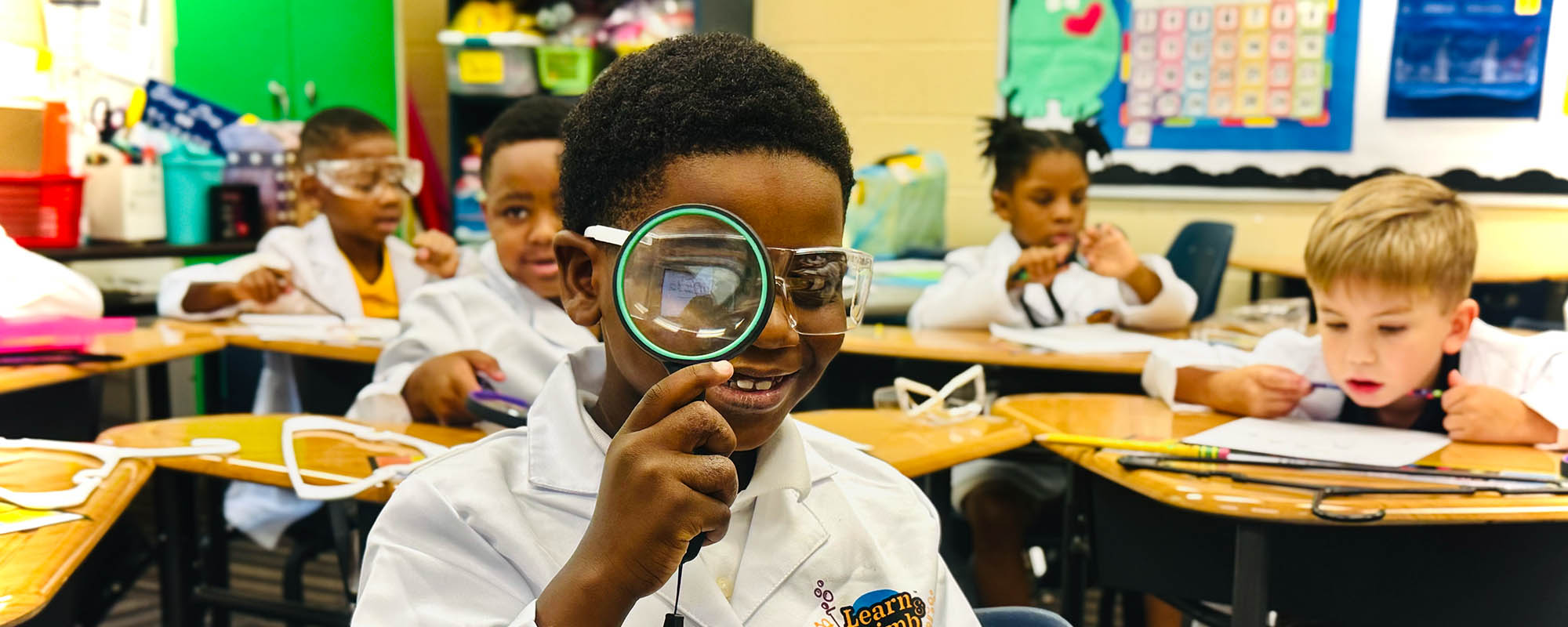 School boy in the classroom holding up a magnifying glass