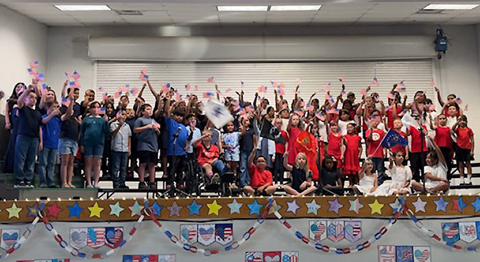 Students on stage holding up mini American flags