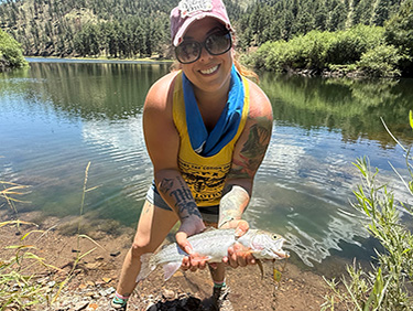 Student by a stream holding a fish she caught