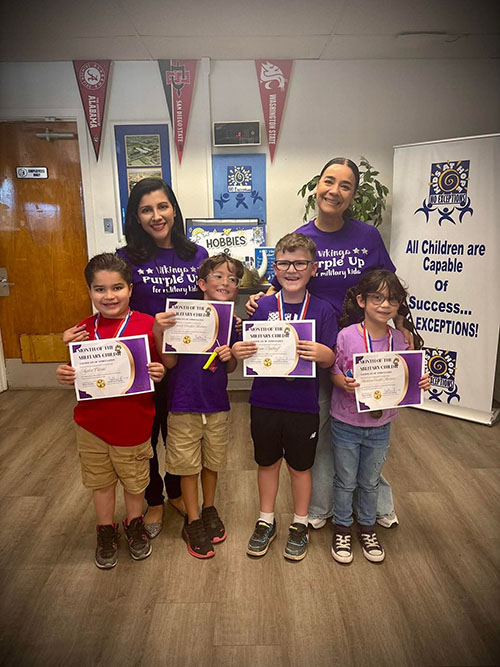 Two women in purple t-shirts with a group of elementary students holding certificates